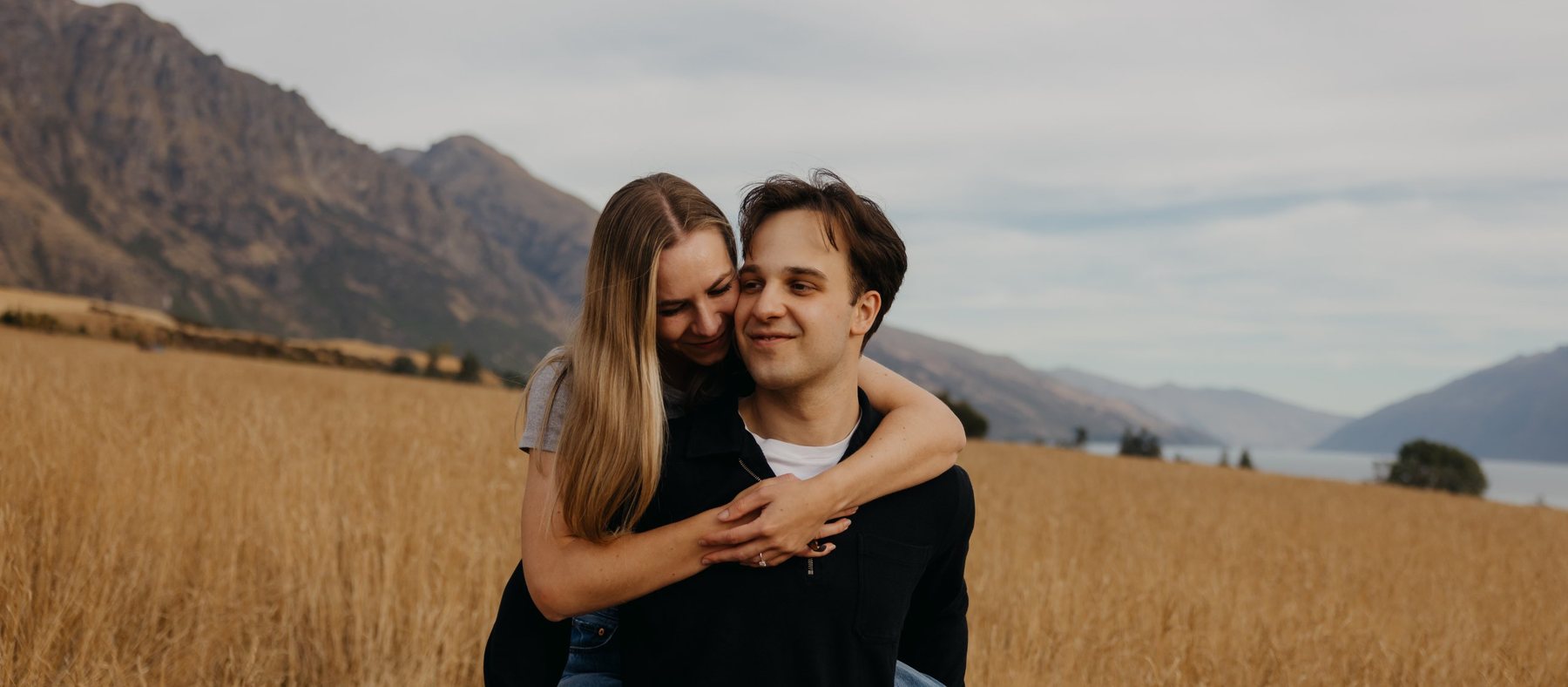 Matia carrying Jillian on his back in a field of golden grass, both smiling